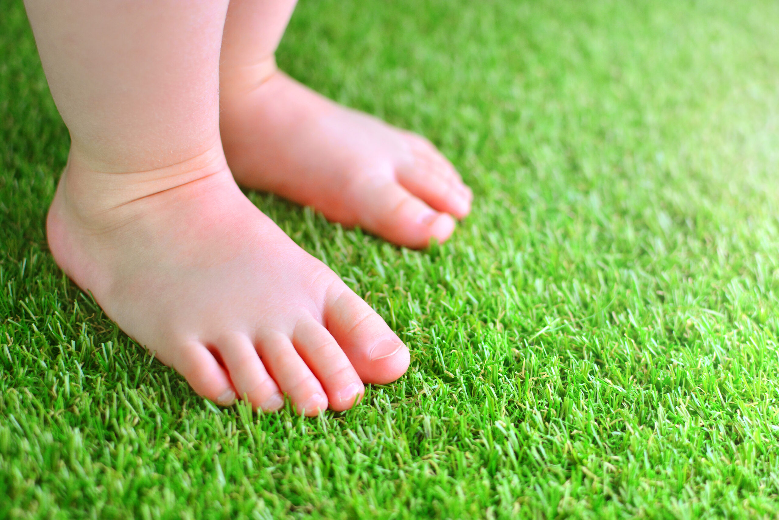 Artificial,Grass,Background.,Tender,Foots,Of,A,Baby,On,A